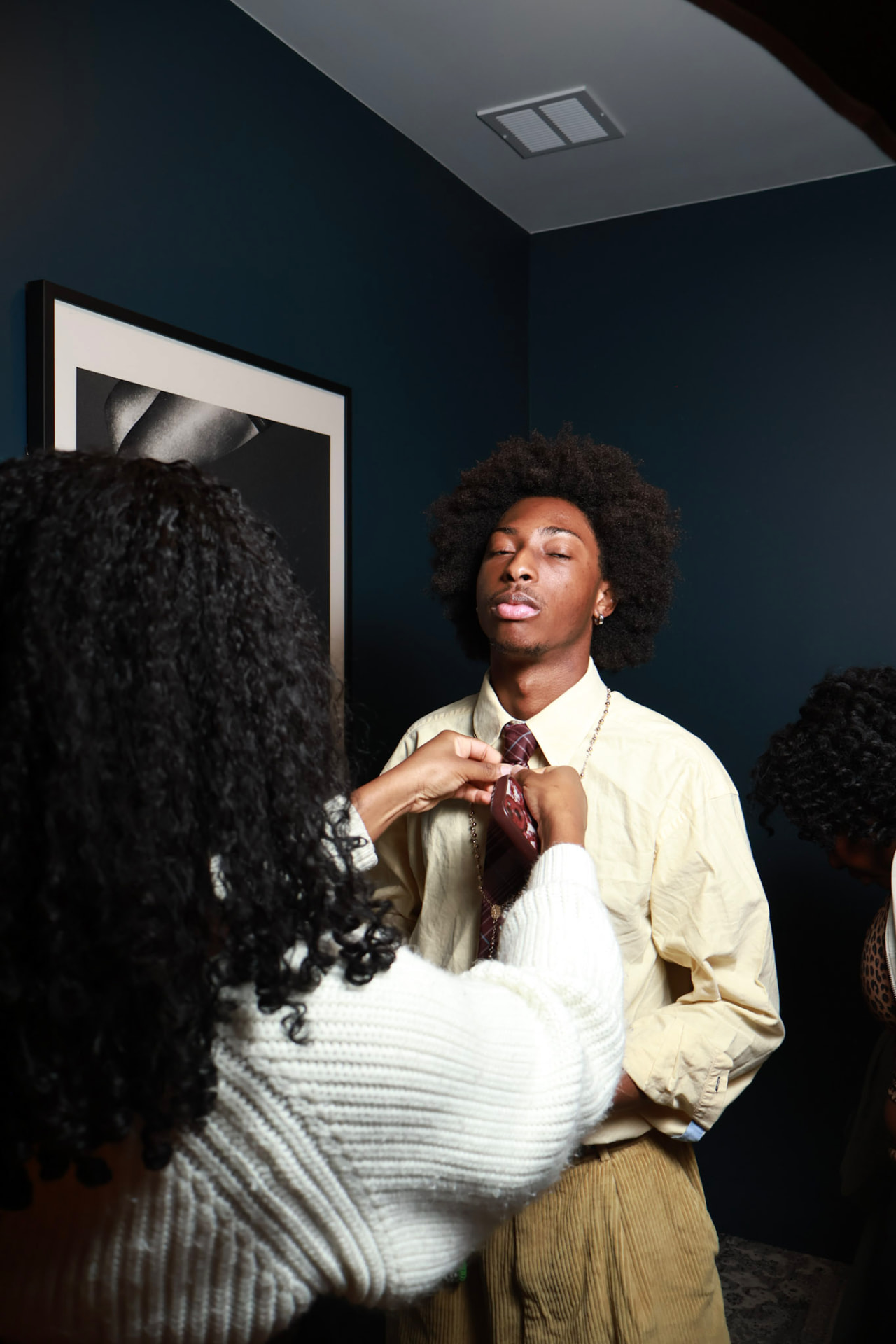 Behind the scenes — a stylist adjusts a model's tie while a third person waits nearby